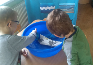 Chłopcy puszczają papierowe łódki w misce ciepłej wody.
